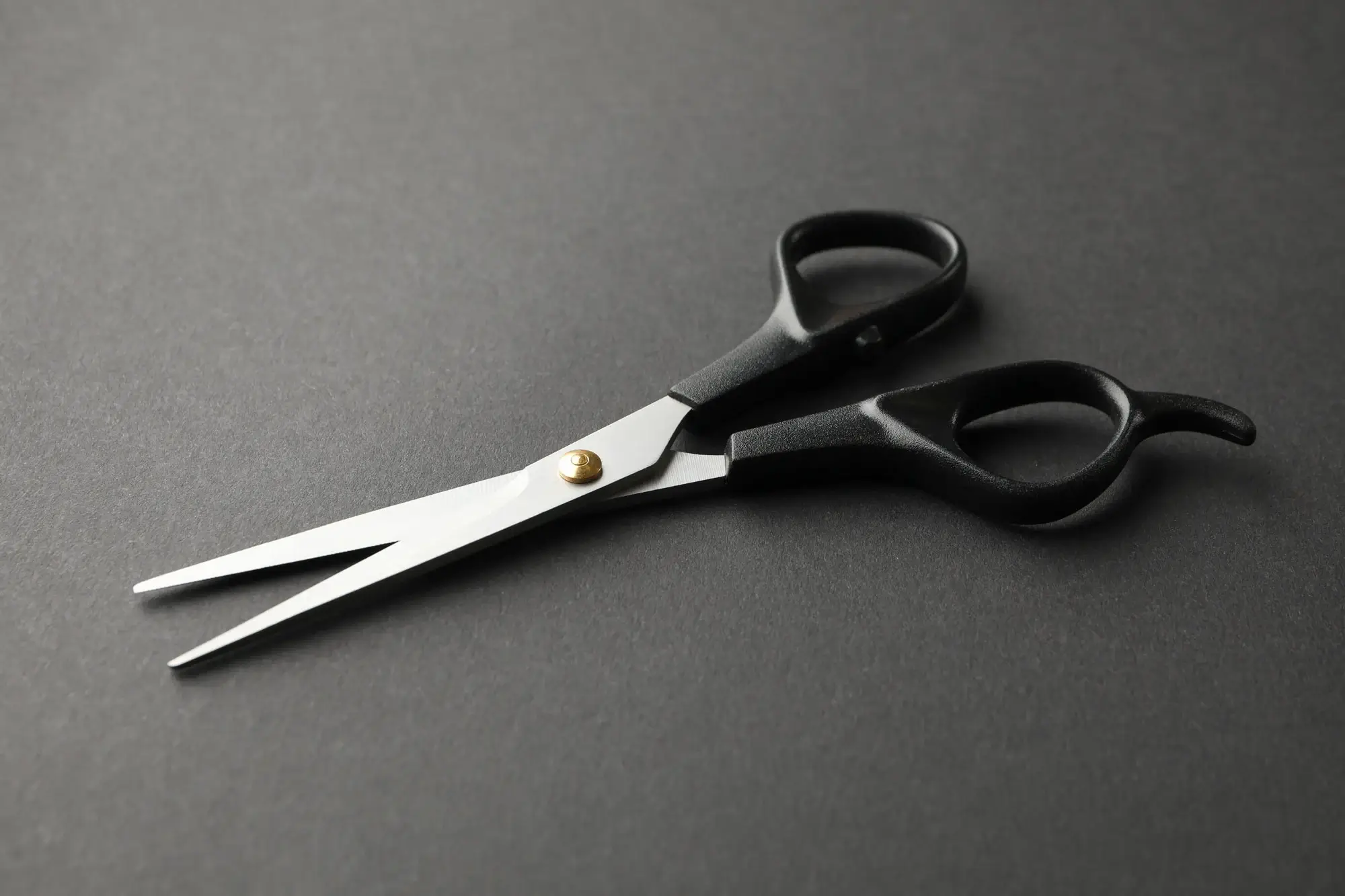 Tijeras de peluquería con mangos negros y hojas plateadas, entreabiertas sobre un fondo gris oscuro