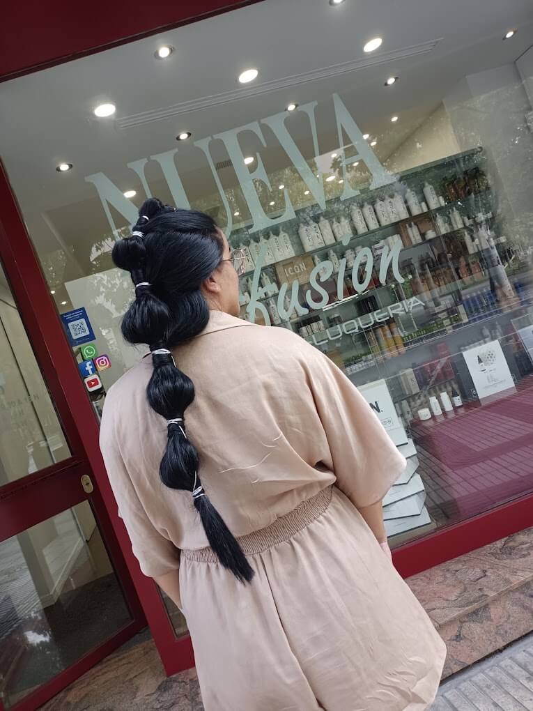 Coleta larga de burbujas en pelo negro, sujeta con gomas a tramos, vista de espaldas ante el escaparate de la peluquería