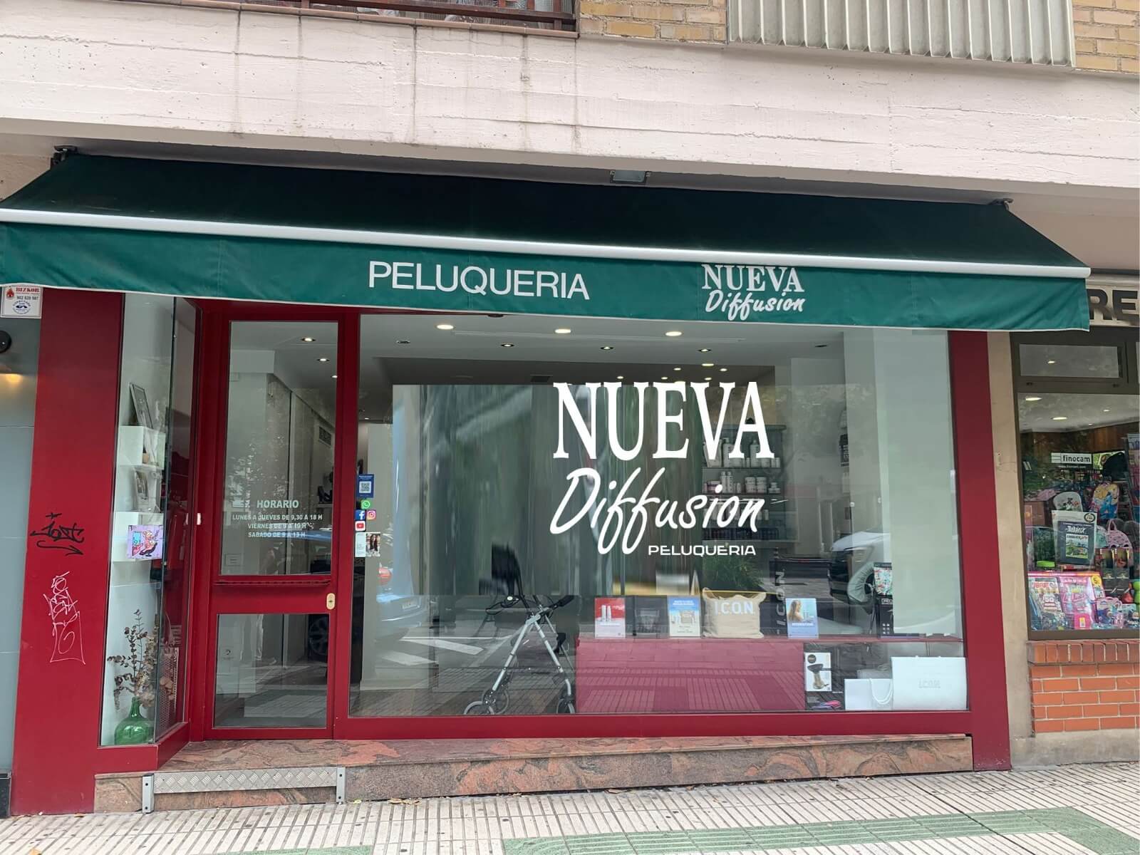 Fachada de la peluquería Nueva Diffusion con toldo verde y escaparate de marco rojo en Iturrama, Pamplona